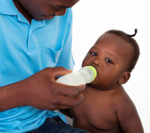 An obese african american baby being bottled fed by his dad for an article titled, "does baby sucking ability lead to obesity? " for successful black parenting magazine.