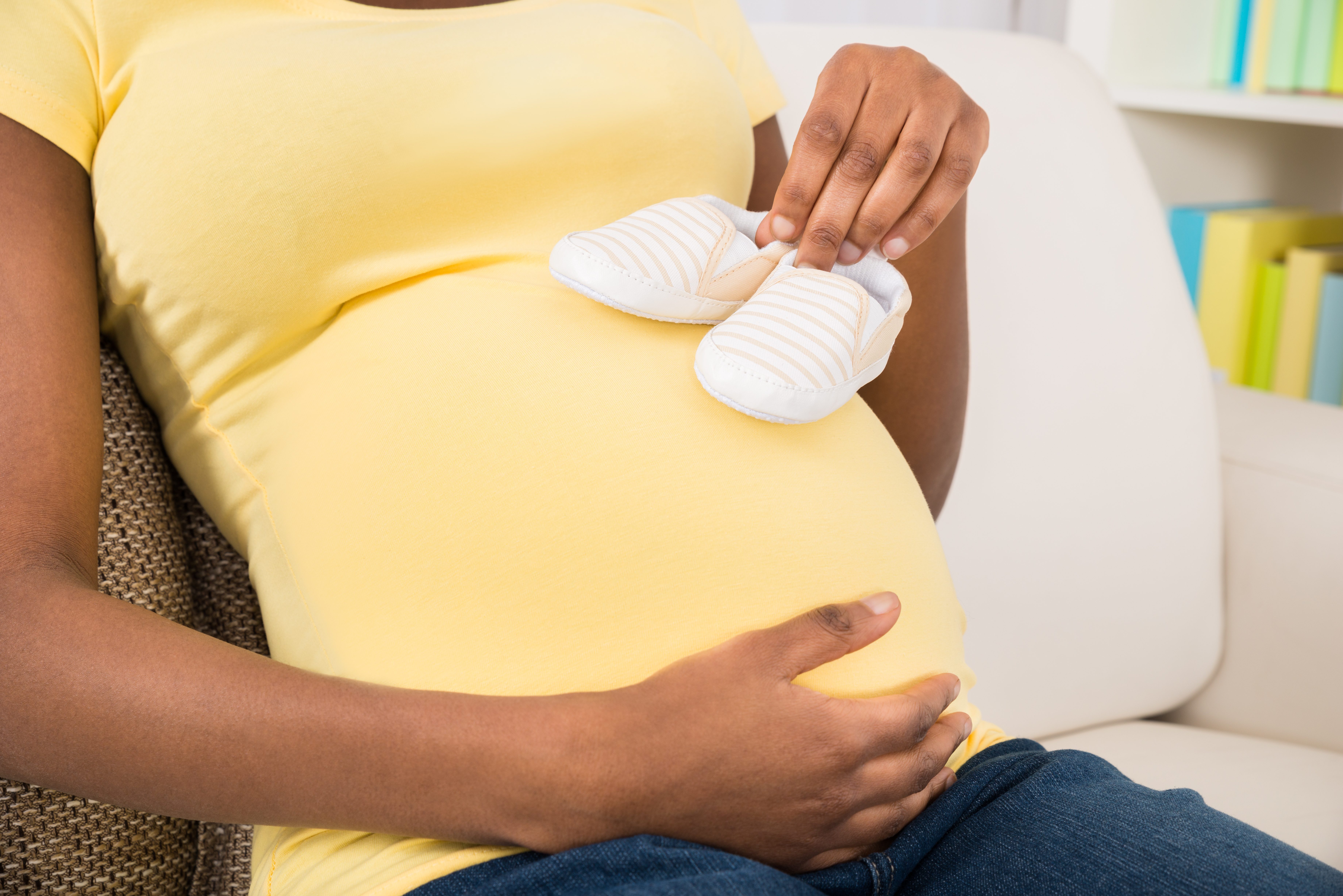 Close-up Of Pregnant Woman Sitting On Sofa Holding Baby Shoes At Home