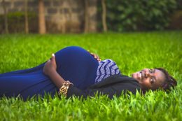 Black pregnant woman laying on the grass in a blue dress for an article helpin women to conceive by successful black parenting fertility