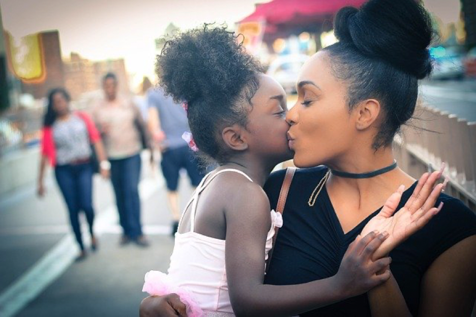 African american mom kissing her young daughter on the forehead.