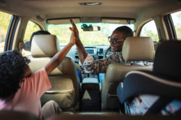 An african american father giving his child a high-five in the car on a road trip. Keep your toddler comfortable on the road.
