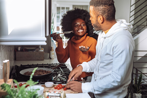 Father and daughter cooking together, tasting the meal-in-progress - african american family bonding in the kitchen