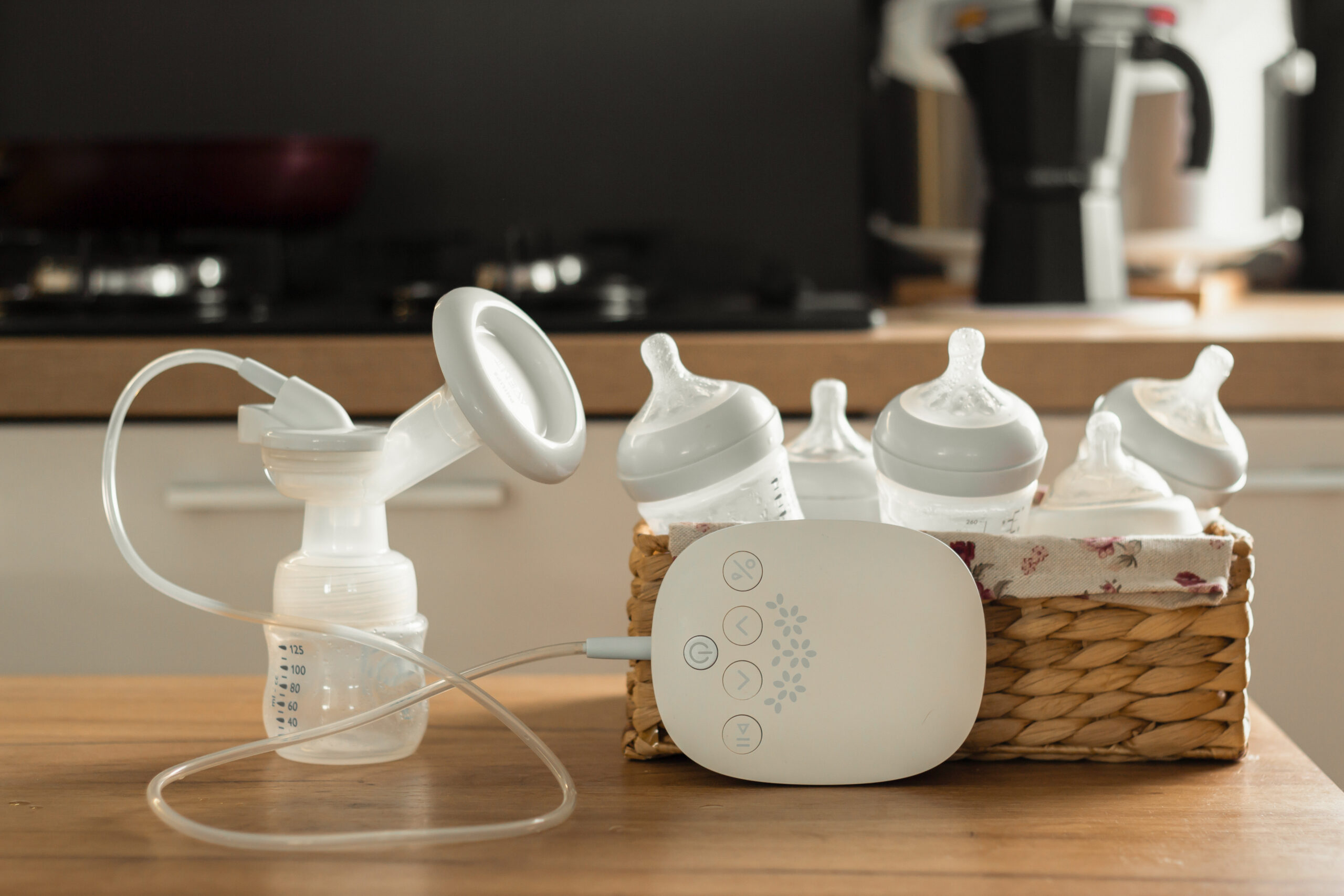 Electric breast pump and bottles for breasting milk in a wicker basket on a wooden table