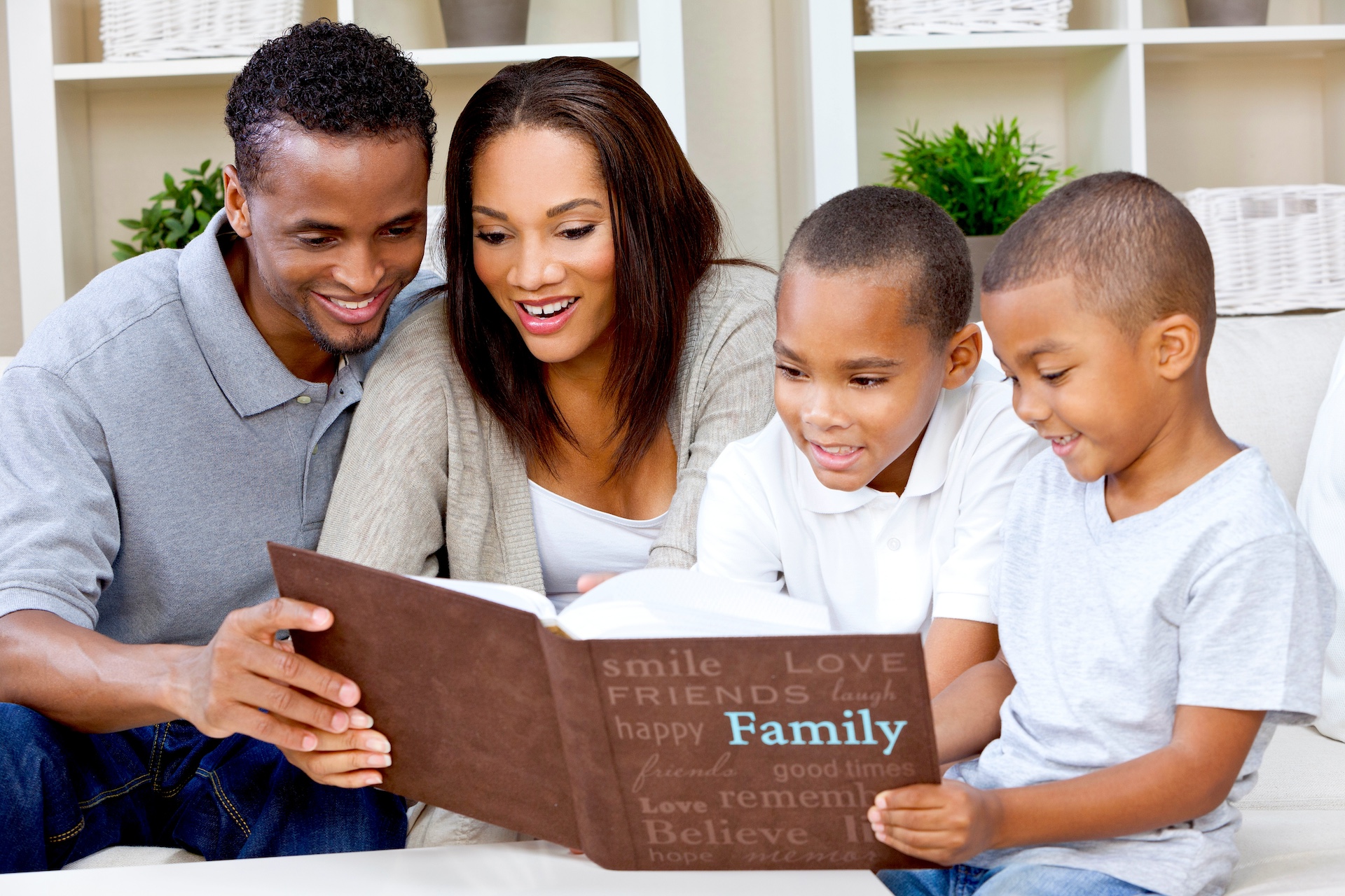 Family of four looking at a travel photo book, smiling and enjoying their time together on a couch.