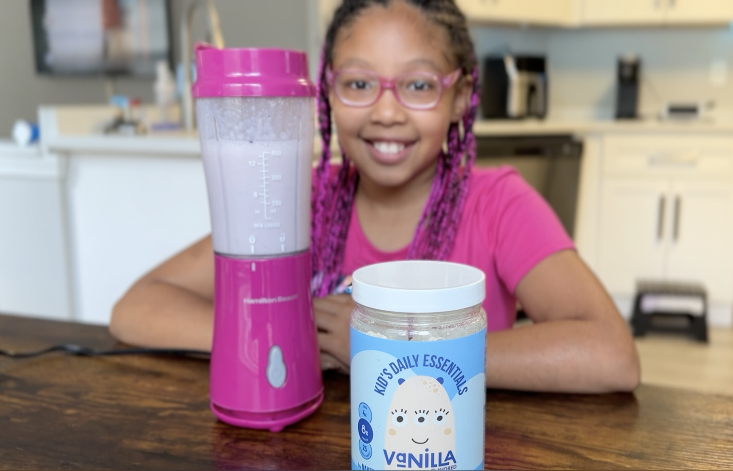 African american girl with pink and black braids makes a protein smoothy from naked nutrition shakes.
