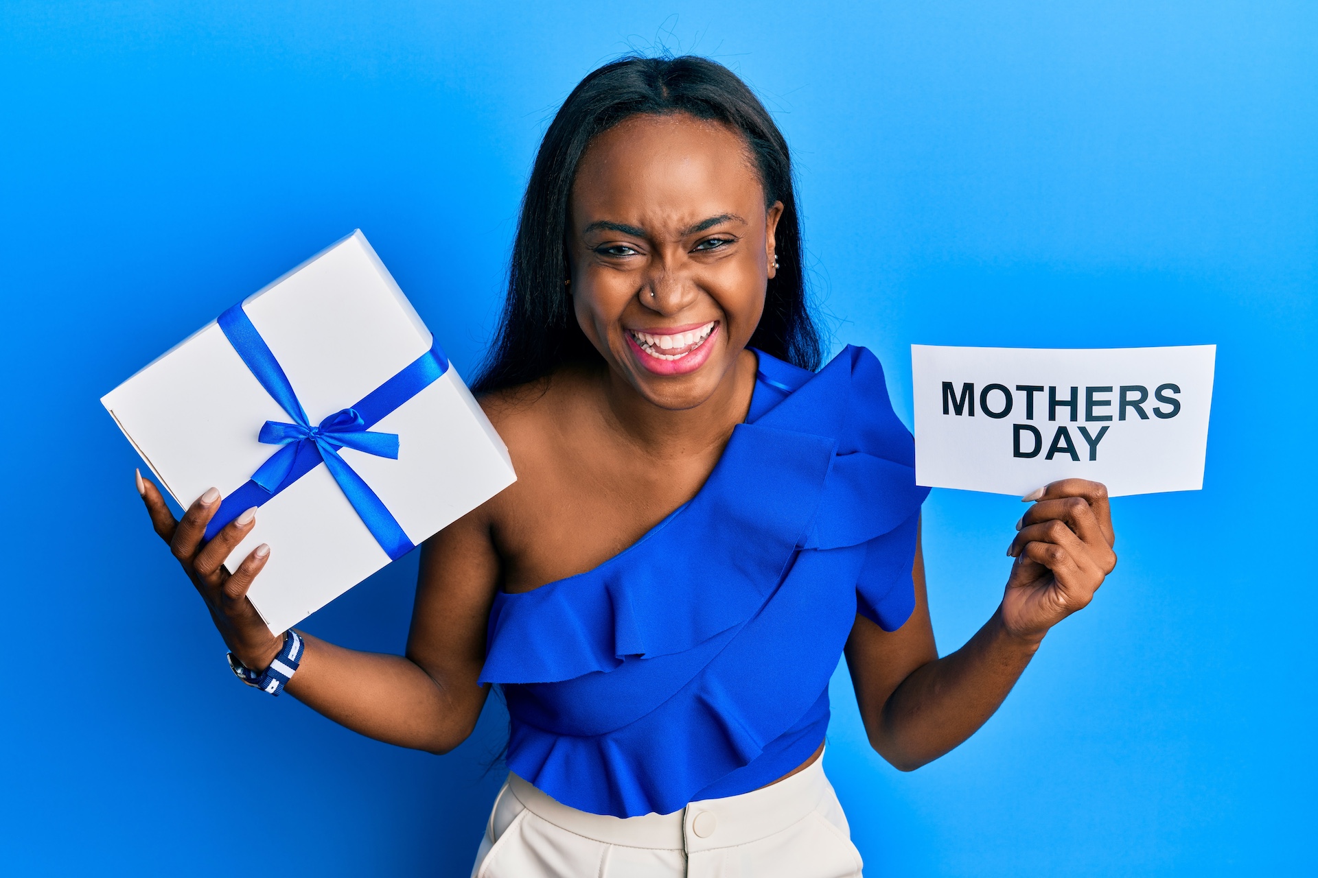 Mother's day, self-care gifts. Young african woman holding gift and mothers day text smiling and laughing hard out loud because funny crazy joke.