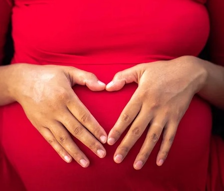 An african american pregnant woman making a heart on her belly for an article on how to get pregnant.