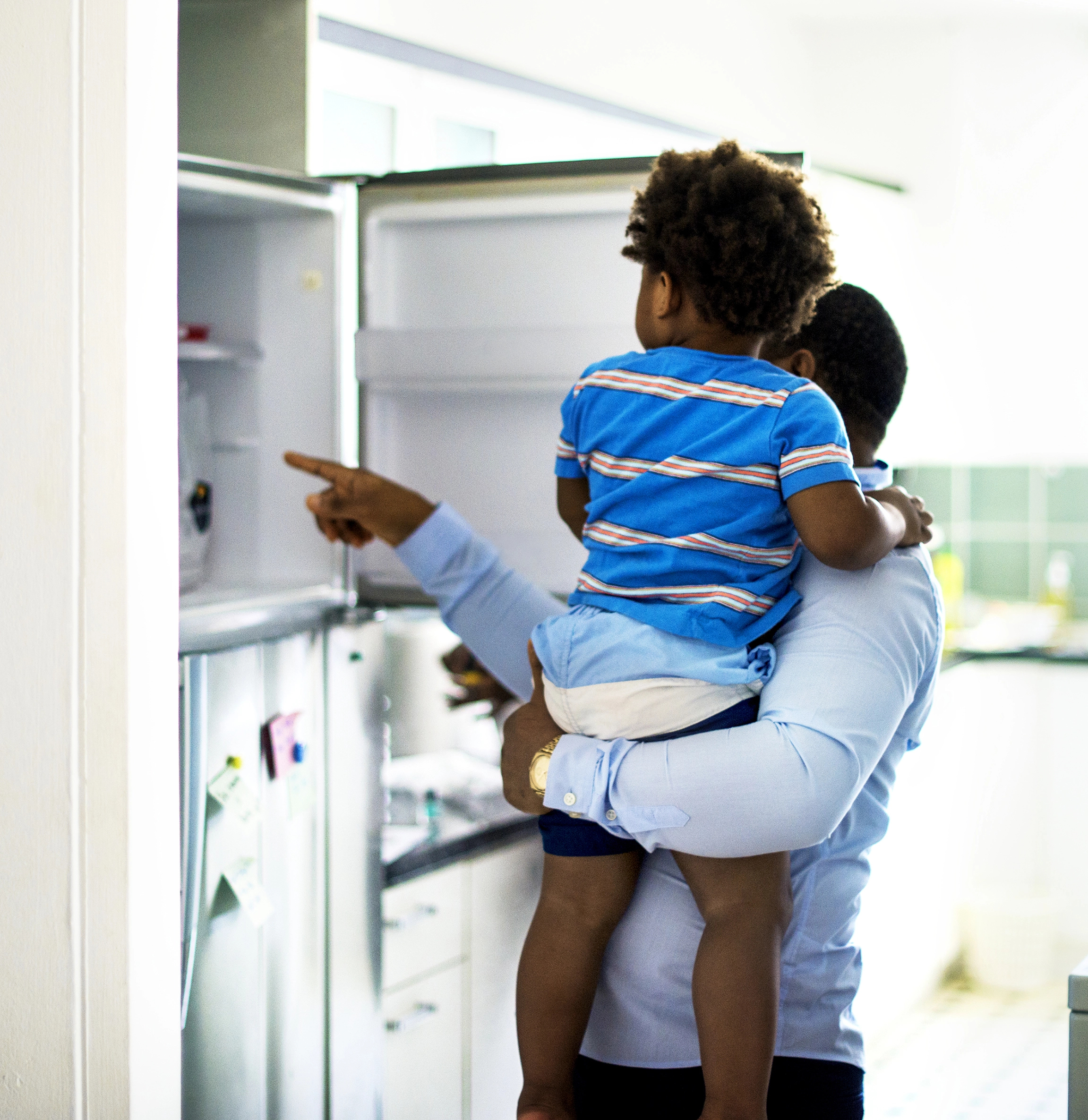 A dad opens the fridgerator with his son while wasting energy by leaving the door open
