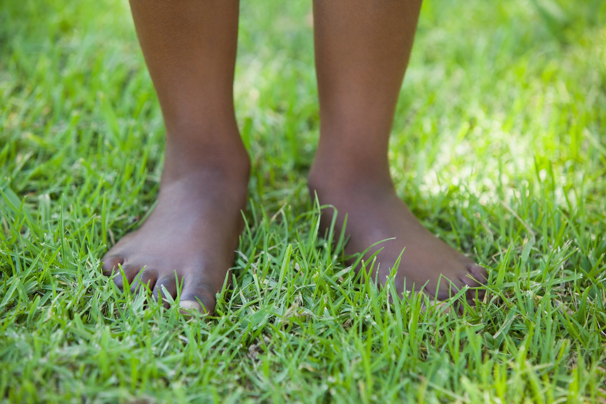 African american child with feet in green grass for reasons why children take off their shoes or walk barefoot.