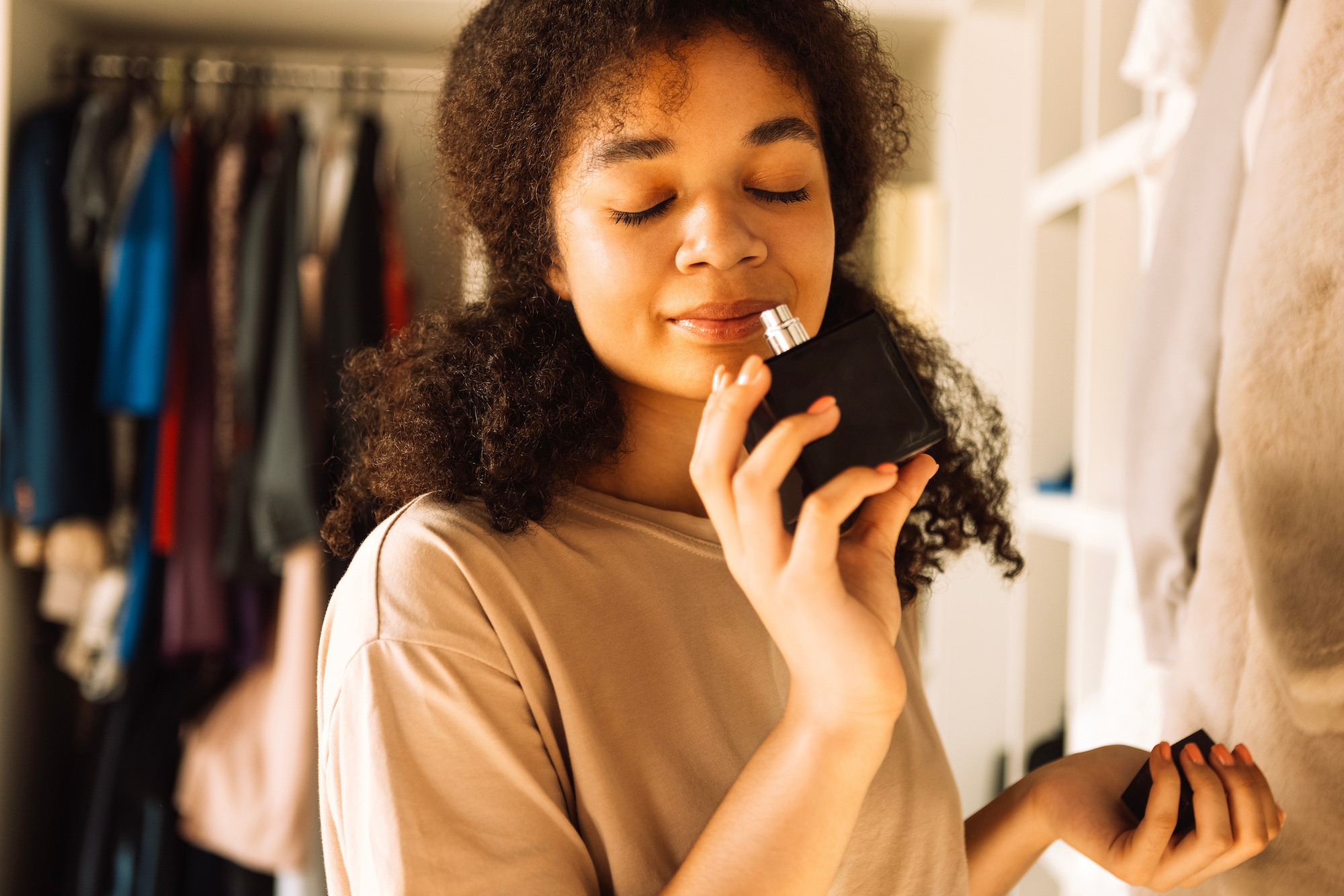 African american teen girl sniffs perfume bottle in her closet for budget-friendly stocking stuffer ideas for black friday.