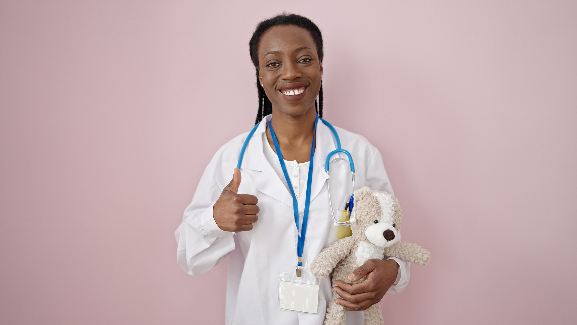An african american nurse with thumbs up and a teddy bear to show that nurses empower parents.