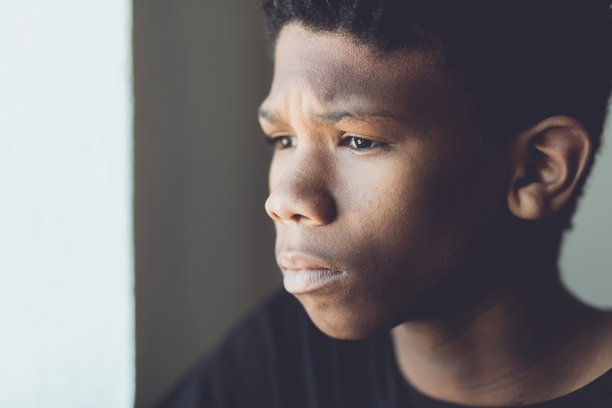 An african american boy looks worried as he look out a window for an article about the long-term effects of boy scout sexual abuse parents should know about