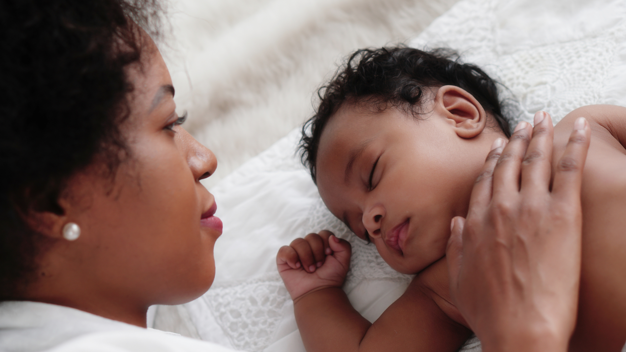 Different sleep behaviors of babies An african american mother watching her baby sleep for an article on sleep behaviors of babies