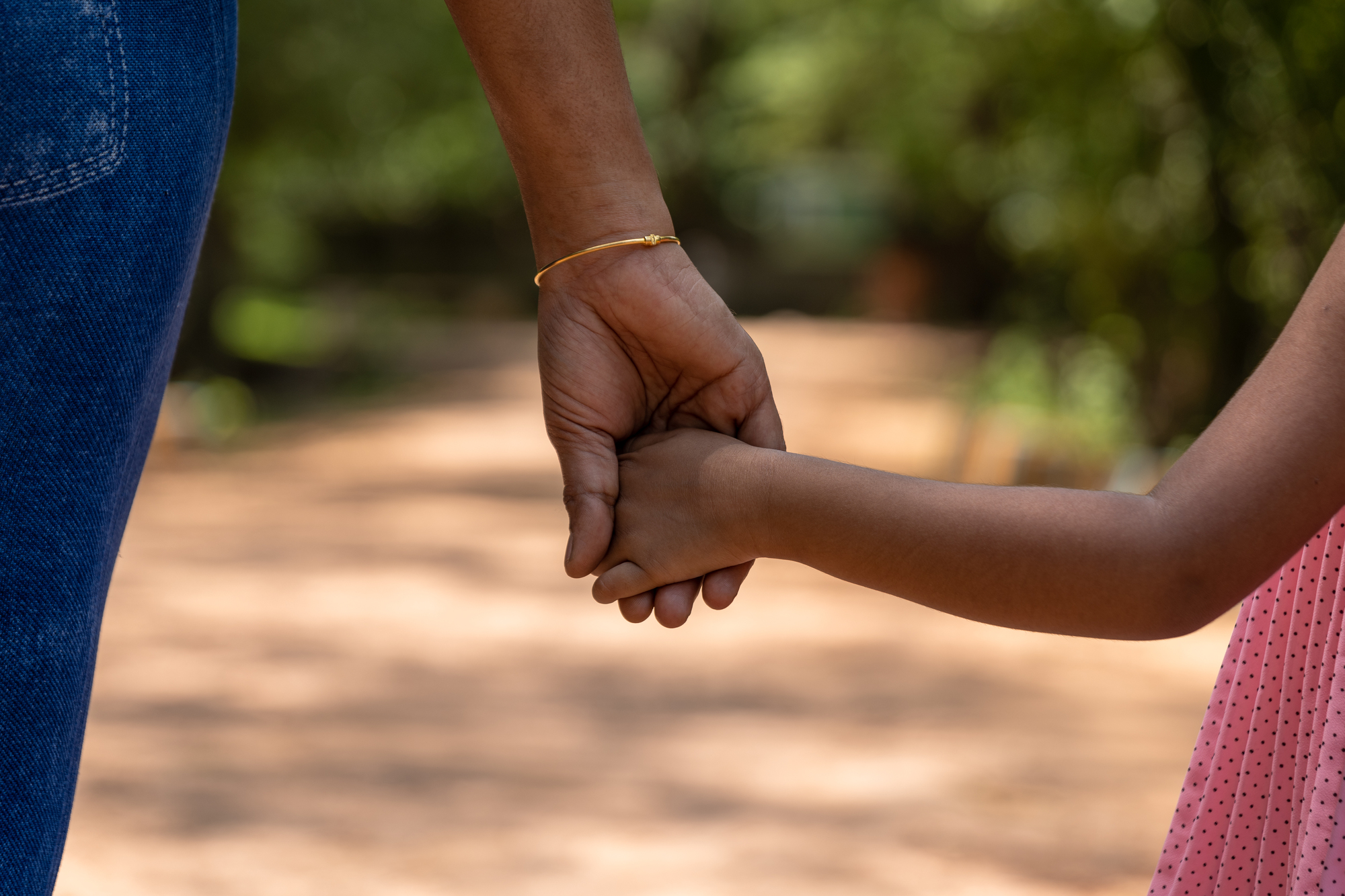 Close-up of an adult holding a child’s hand, symbolizing parental care and child support responsibilities, with a blurred natural background representing guidance and stability after separation for an article on child support.