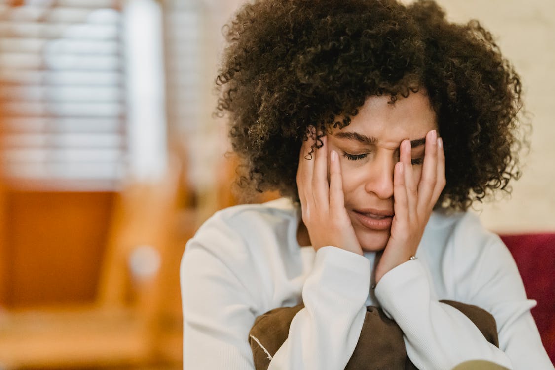 A black mother sits in distress with her head in her hands, illustrating emotional struggle and mental health awareness. This image represents the silent battles many black parents face while navigating bipolar disorder in the family.