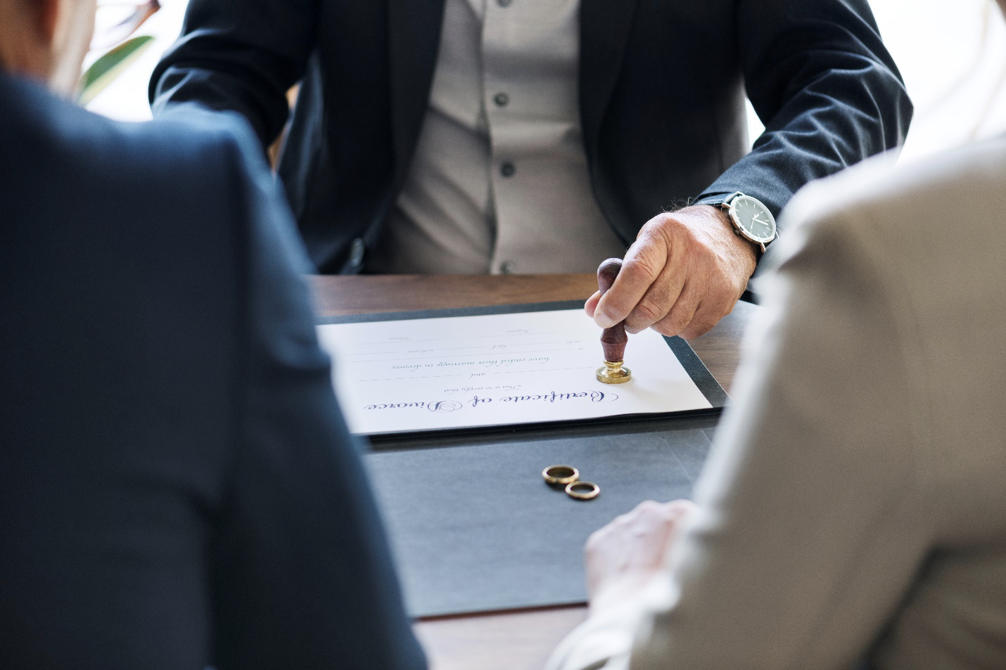Divorce attorney in orange county stamping a certificate of divorce with wedding rings on the table between separating couple during legal proceedings to dissolve their marriage.