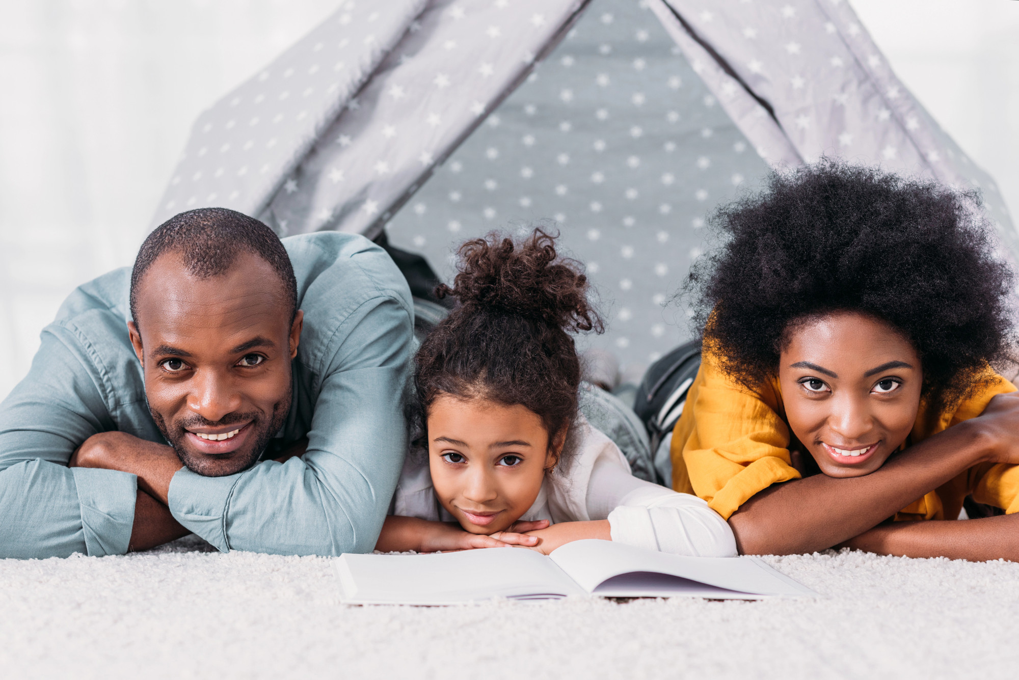 Black family smiling and bonding together while reading a book inside a cozy tent, symbolizing connection and conscious parenting at home for an articel about good parents aren’t born, they adjust.