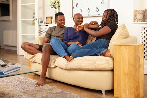Black family sitting together on a couch at home sharing a warm moment of connection and support during mental health recovery, healing together in a safe family environment