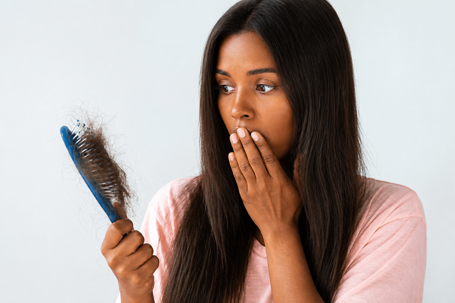 African american woman brushing her long, straight black hair while checking for signs of a thinning crown and crown hair loss.